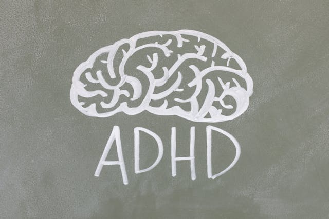 A chalk drawing of a brain with the letters "ADHD" written underneath on a green chalkboard.